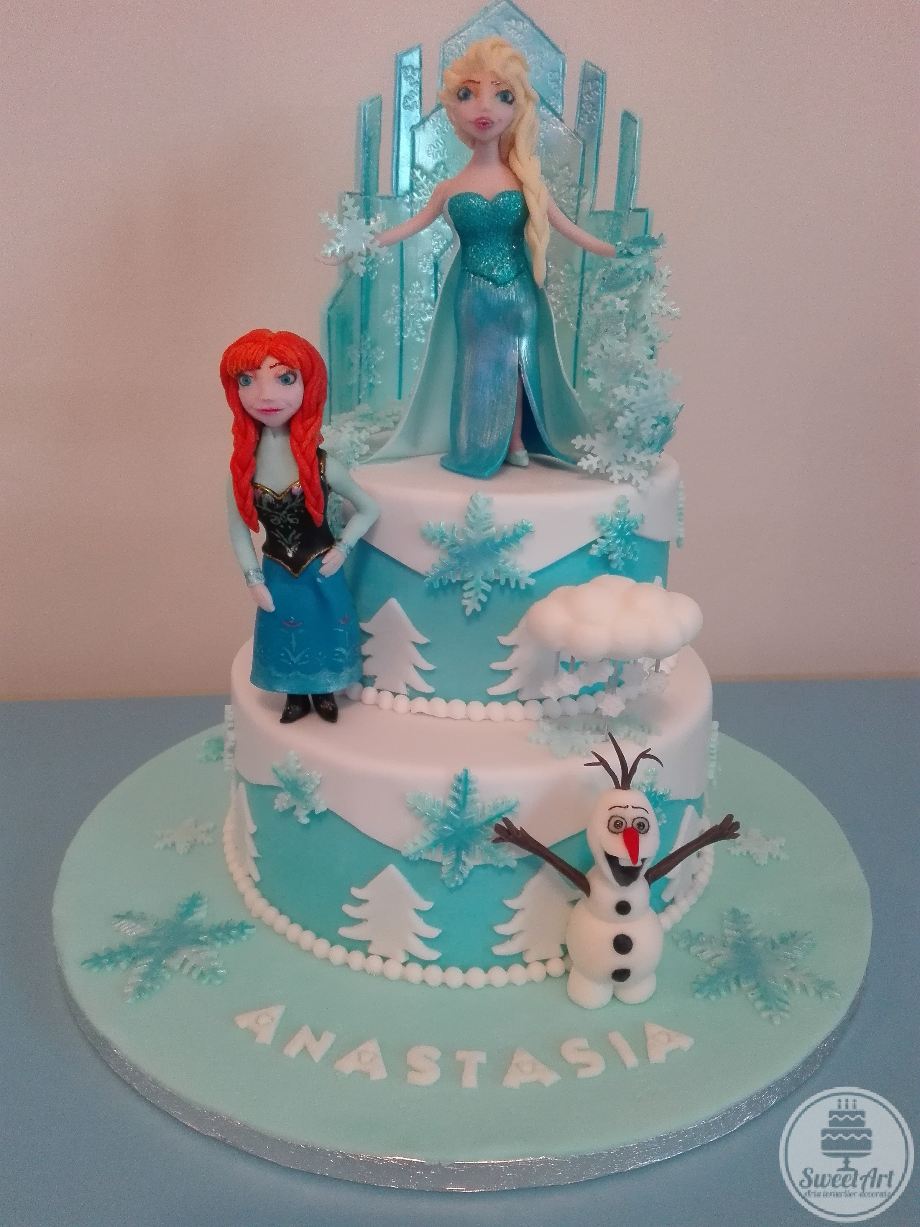Tort Frozen Regatul de gheață: Elsa - regina gheții cu vraja ei care îngheață şi castelul de gheață, sora ei prințesa Anna, Olaf - omul de zăpadă şi norişorul lui, brazi, mărgele şi fulgi de zăpadă