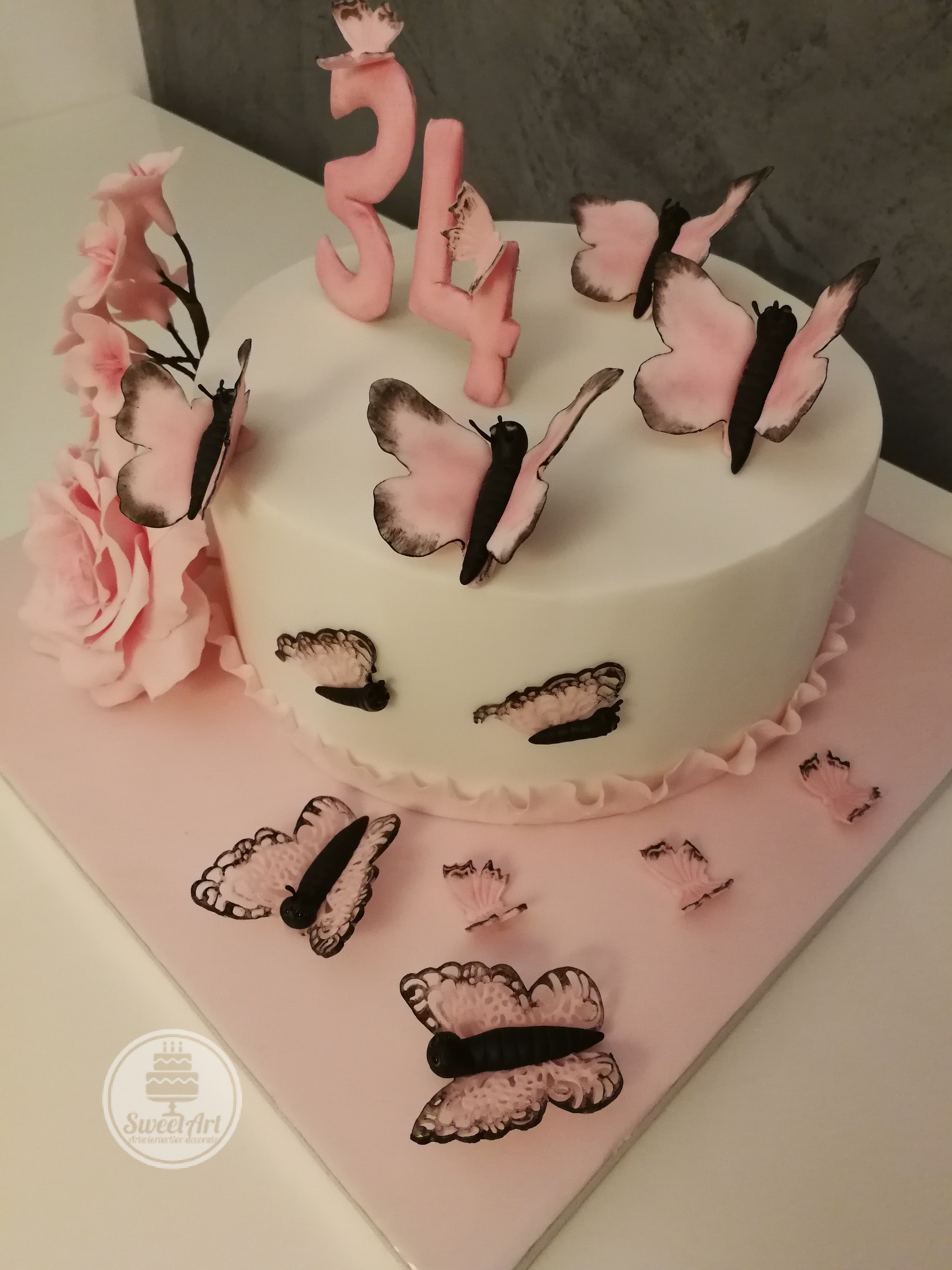 Tort cu fluturi și flori: fluturi fluturași simpli și dantelați roz cu negru, un trandafir roz și o crenguță cu flori de cireș, tort alb-roz-negru cu volănaș - ruffle roz